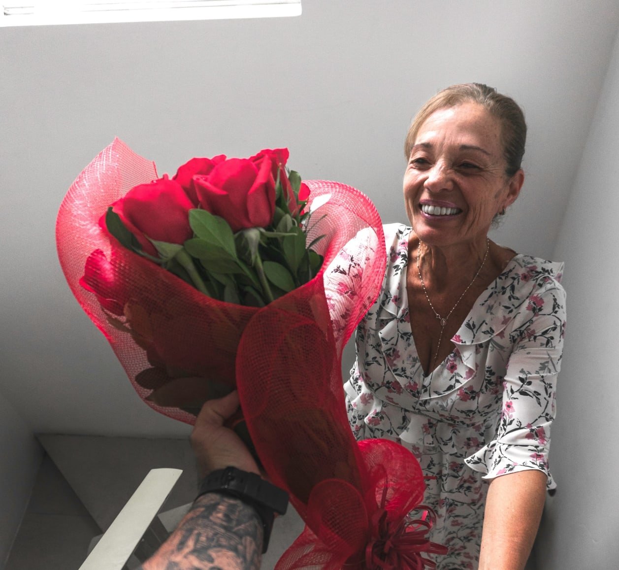 A woman smiles as she receives a large bunch of red flowers