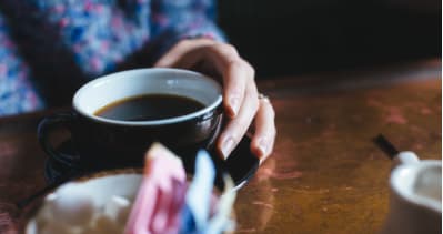 Close-up of a hand holding a cup of coffee on a wooden table